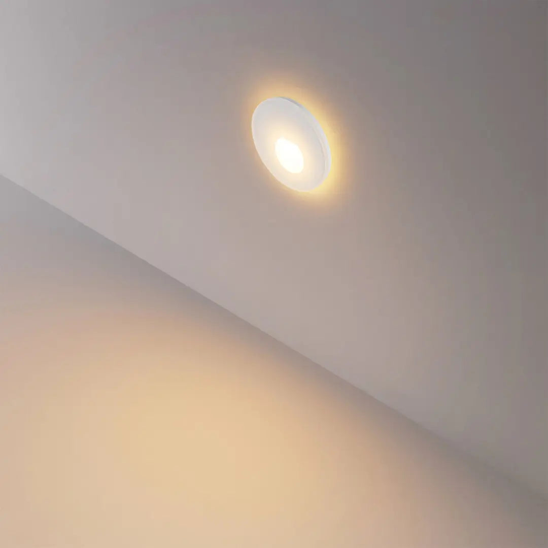 Rond wit glaskapje gemonteerd in de wand naast de trap