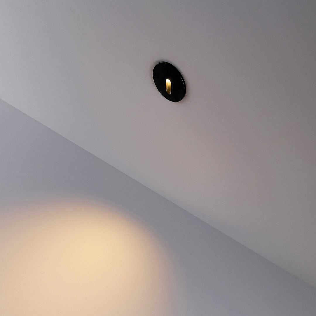Rond zwart kapje gemonteerd in de wand, smalle lichtbundel naar beneden